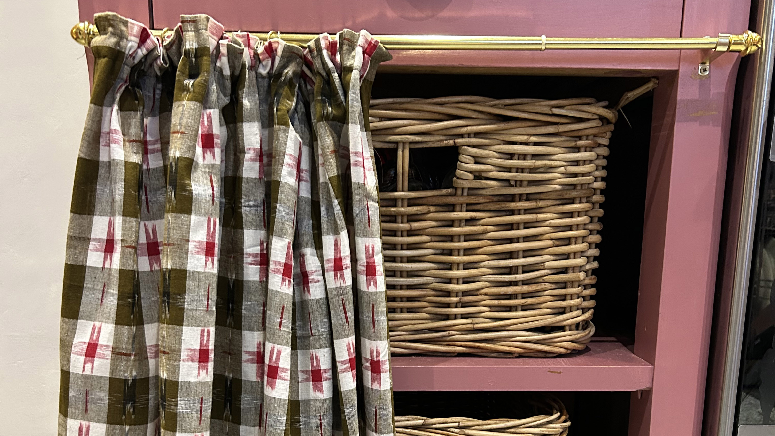 pink kitchen cabinet with patterned curtain across the front