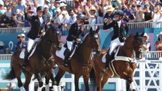 The British eventing team of three riders enjoy their victory lap at the Paris Olympics with the packed stands in the background.