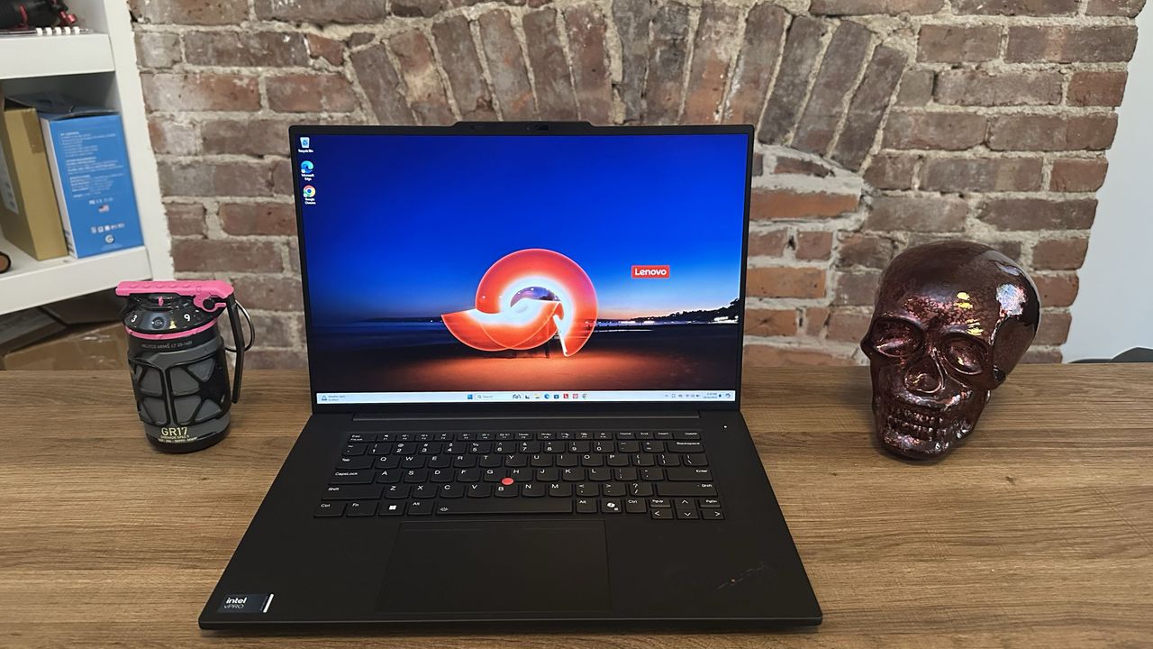 A black laptop on top of a wooden desk with the lid open and showing a colorful, orange and blue image on the screen.