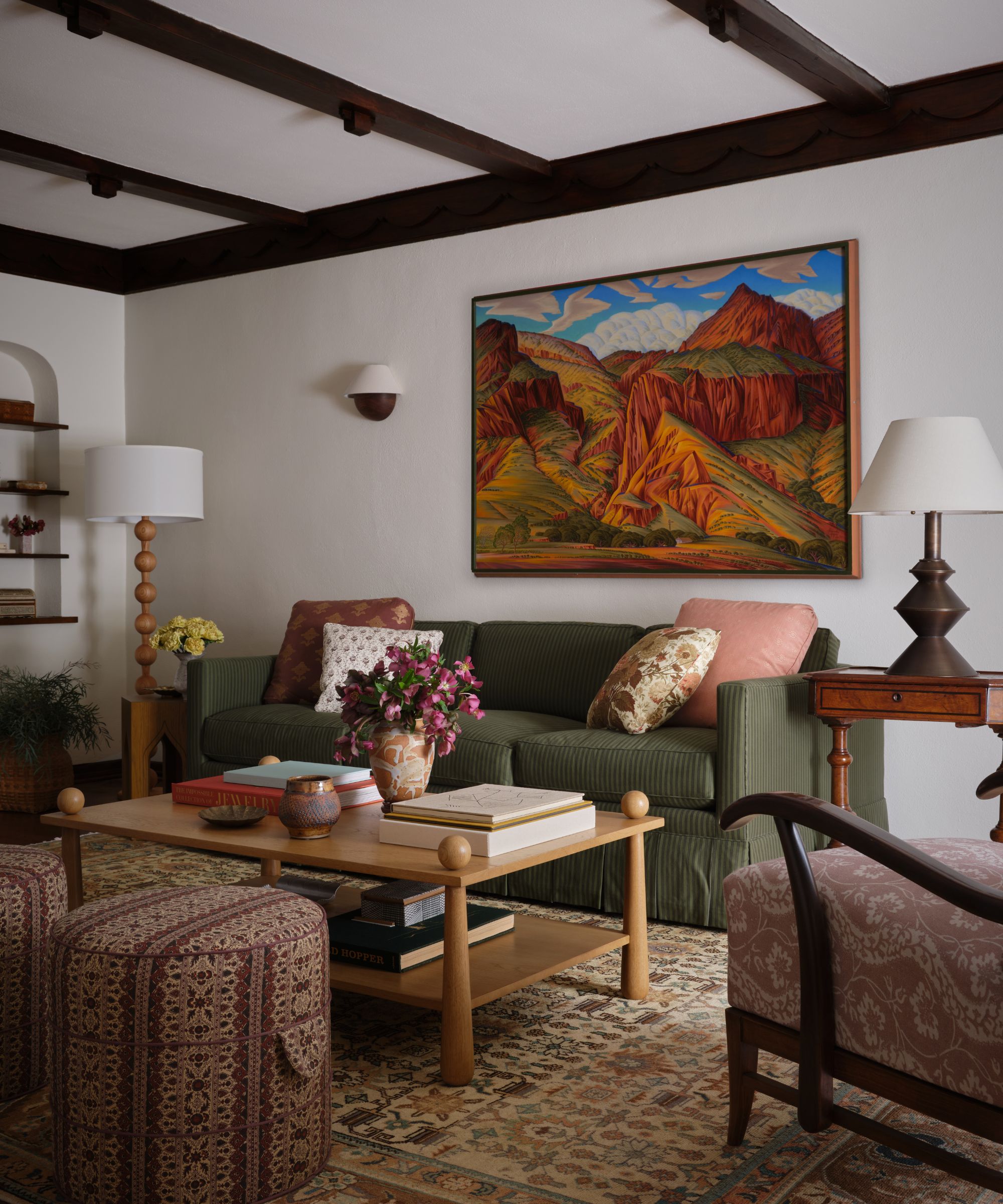 A vibrant living room featuring a large colorful mountain painting above a green sofa, accented by patterned ottomans and a wooden coffee table