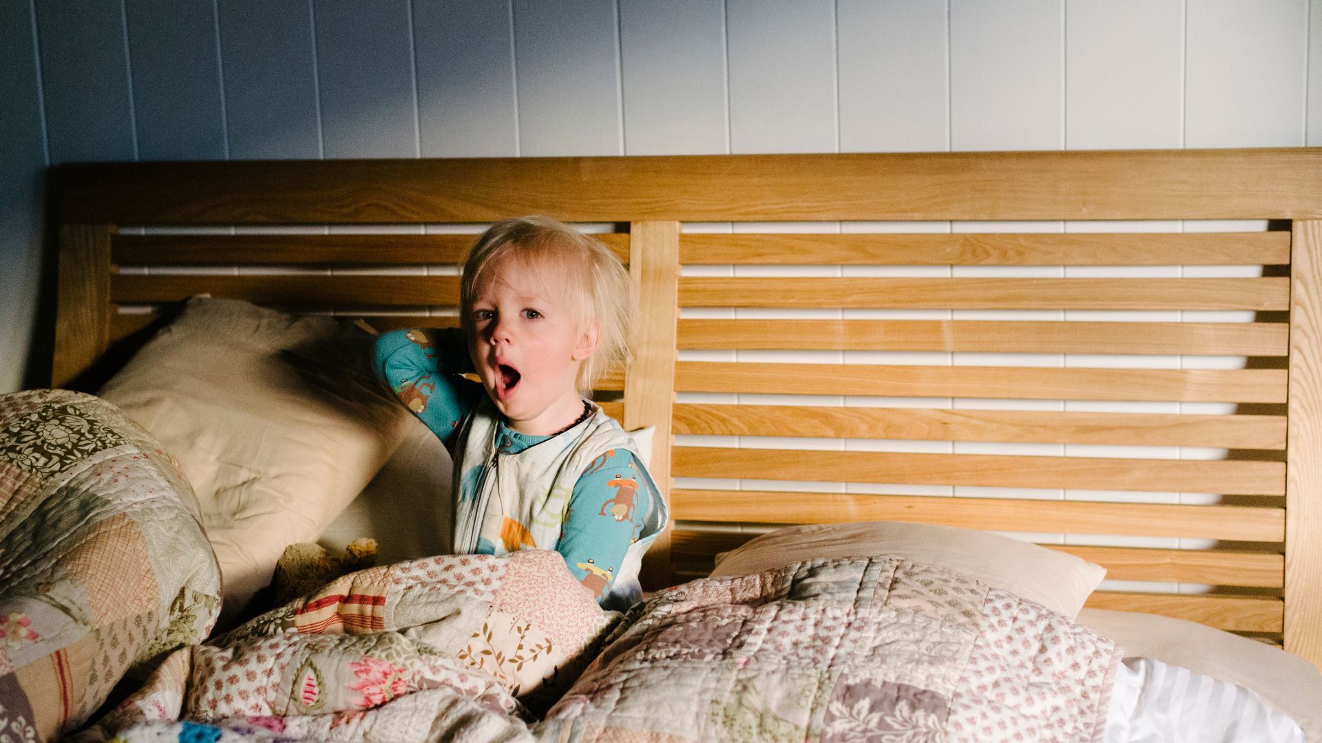 A young child sits up in bed yawning early in the morning.