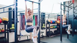 Woman performs hanging knee raise on pull-up bar in gym