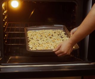 Person puts tray of pumpkin seeds into an oven.