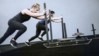 Women performing sled push leg exercise in gym