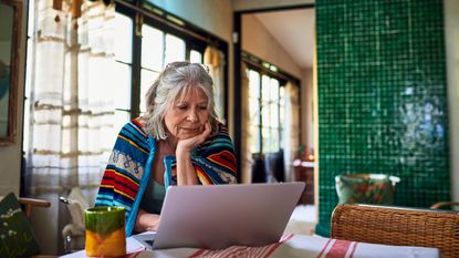 An older woman works on her laptop at home.