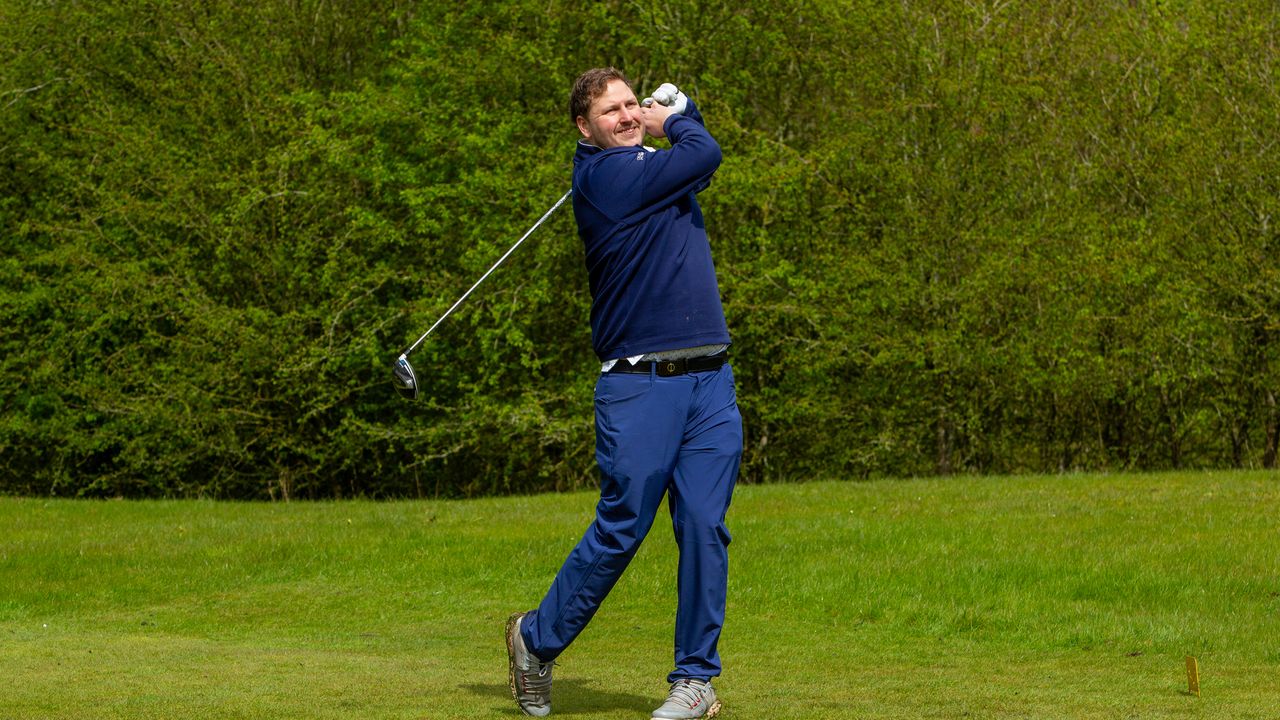 A golfer wearing navy blue holds their finish on a drive