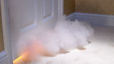 Smoke billows under a closed door into a bedroom.