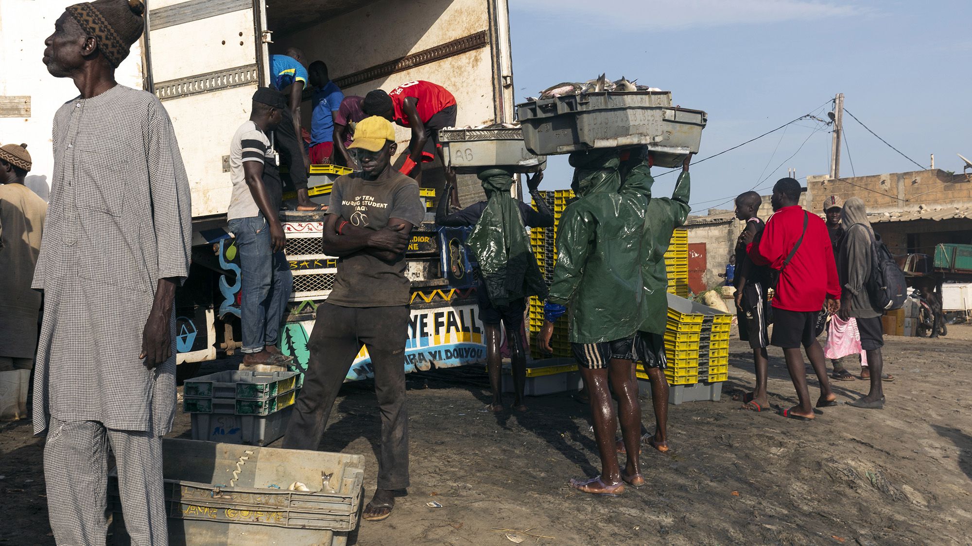A line of people is seen at a local market with baskets of fish nearby.