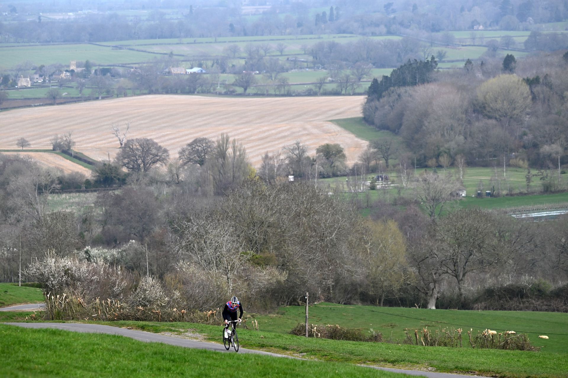 Simon Warren riding on a country road, a wide expanse of Cotswolds countryside behind him