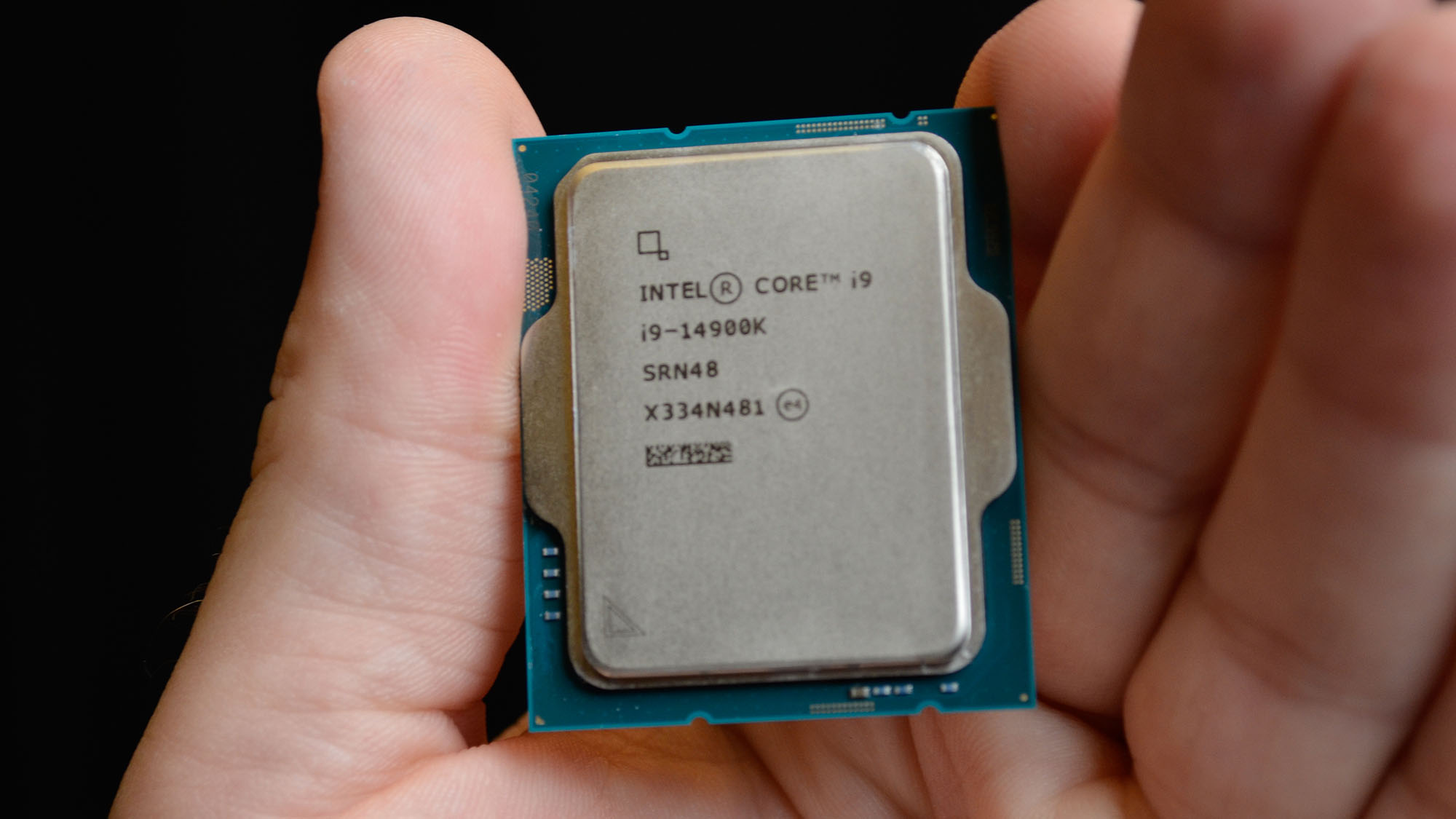 A masculine hand holding an Intel Core i9-14900K