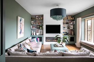 Living room with green walls, wooden floor and large L shaped grey sofa.