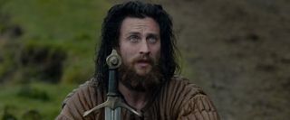 Outlaw King Aaron Taylor-Johnson kneeling with a sword held in front of him