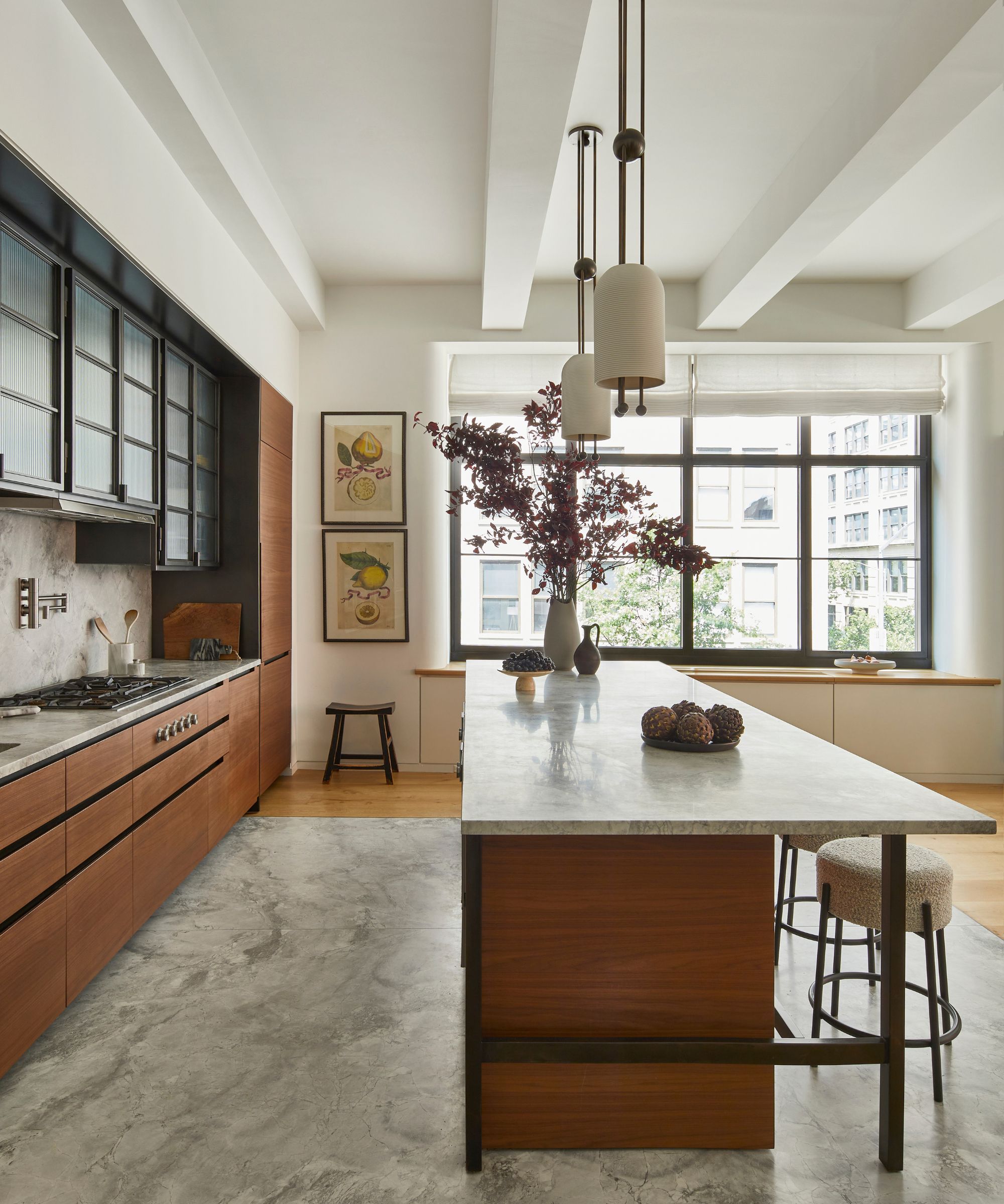 Minimal kitchen with dark wood cabinetry, marble countertop, marbel flooring, kitchen island decorated with vase and ornaments, windows and artwork in background