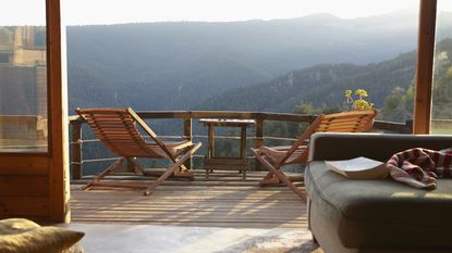 Two chairs sit on the deck of a vacation home facing a view of a mountain in the distance.