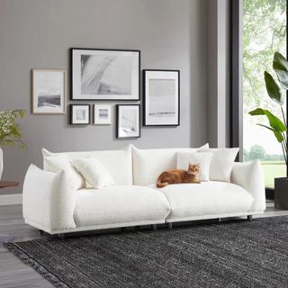A white sofa in a gray room with an orange cat sitting on top