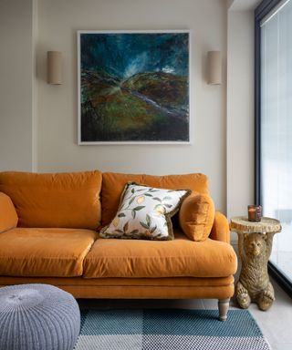 Orange sofa in cream living room, blue rug and artwork, blue pouf