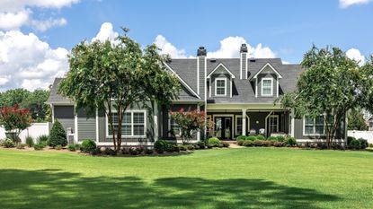 A large gray craftsman house with a large green front lawn