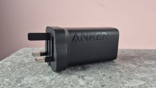 Anker 335 Charger (67W) on stone surface against pink background