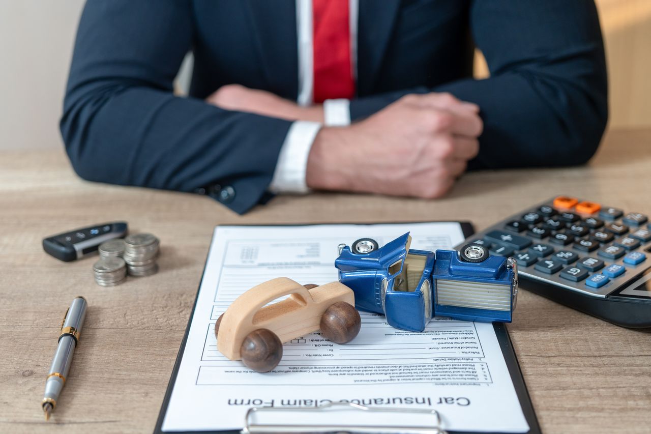 Man paying his car insurance on a desk with a calculator and toy car