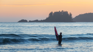 A surfer stands with his surfboard in the water at Chesterman Beach, Tofino.