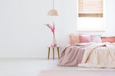 A bed with pink bedding and pink pillows next to a coffee table.