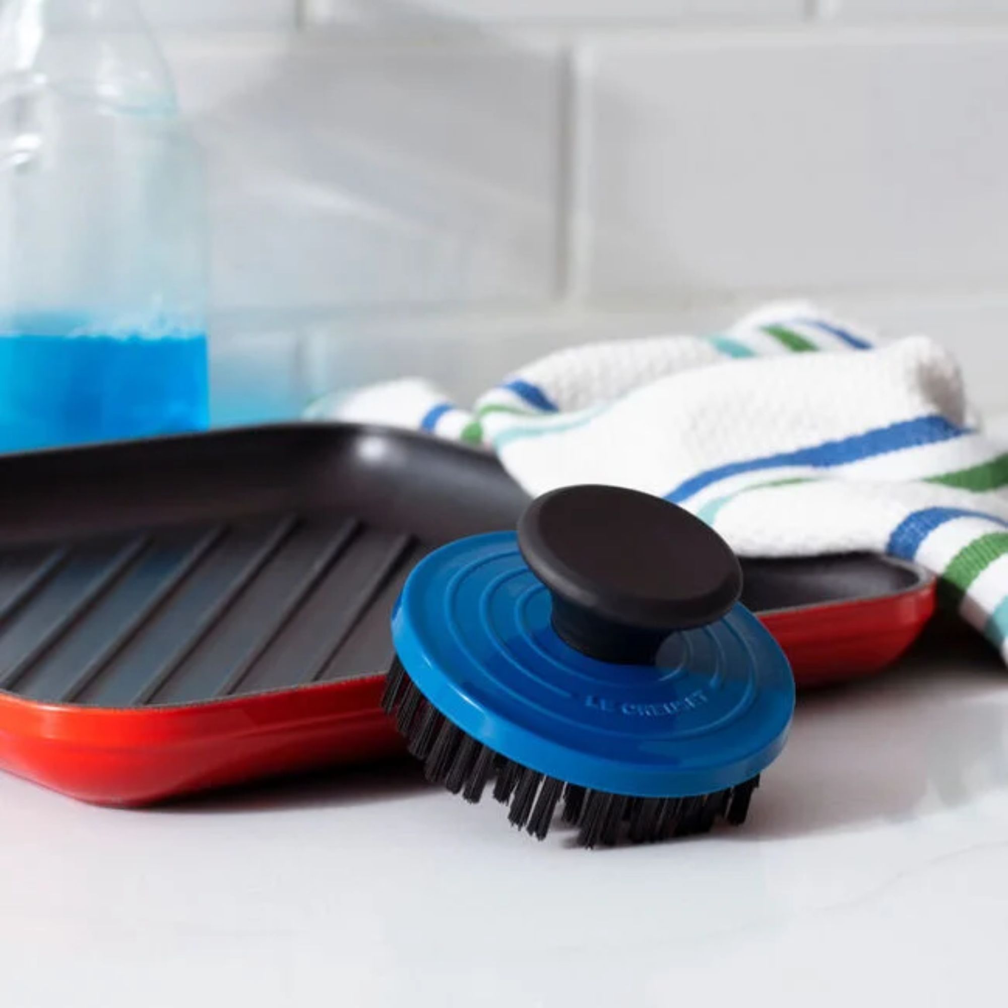 A round blue brush leaning against a red grill pan
