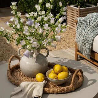 A vase of white flowers on a basket with a bowl of lemons