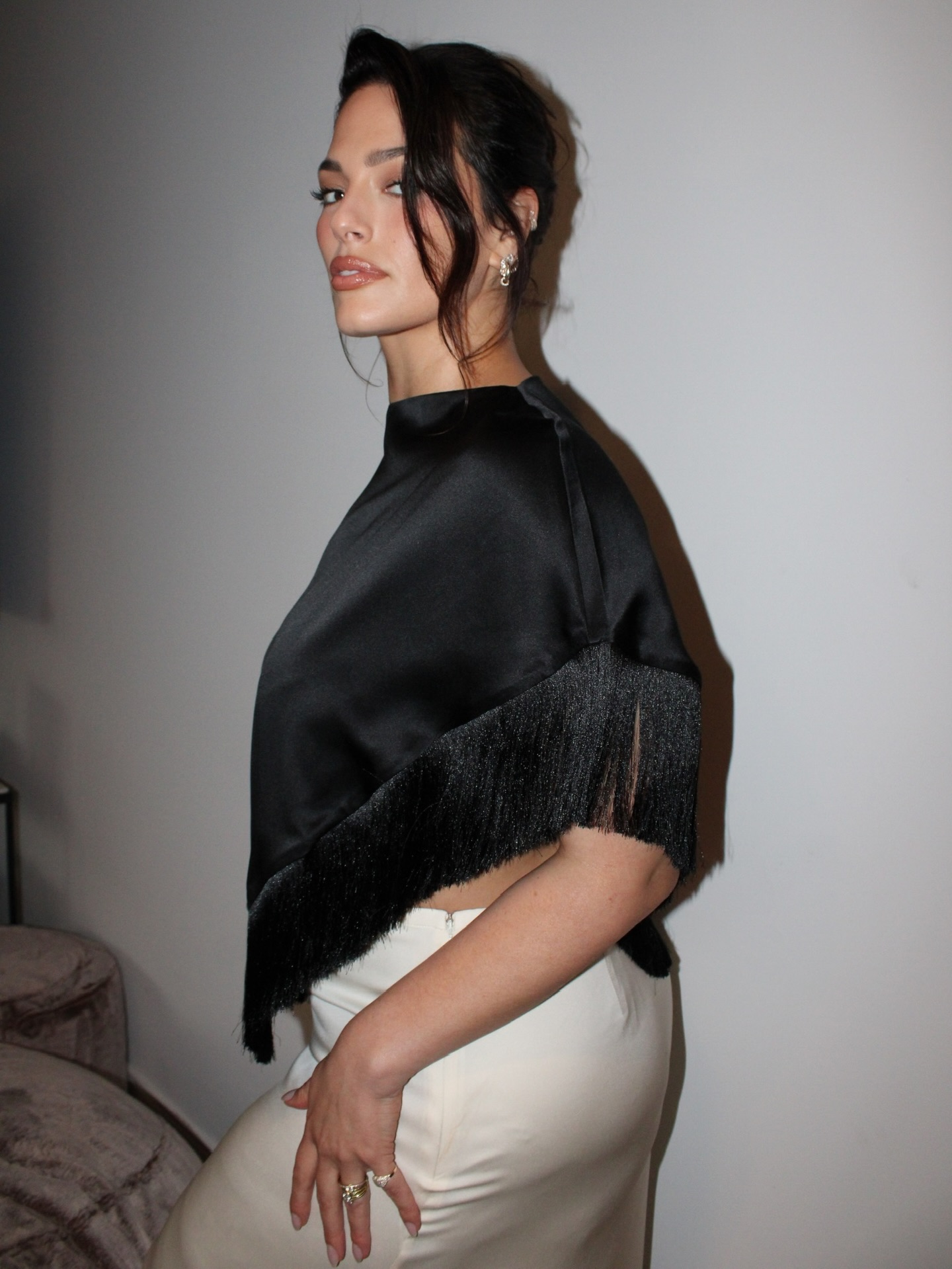 Photo of Ashley Graham posing to the side wearing a black top and white skirt