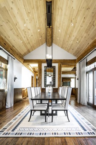 dining room with vaulted ceiling, wood panelling and beams, wooden floor, dining table and chairs, white walls, rug