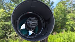 a black and white telescope in a field with trees behind it