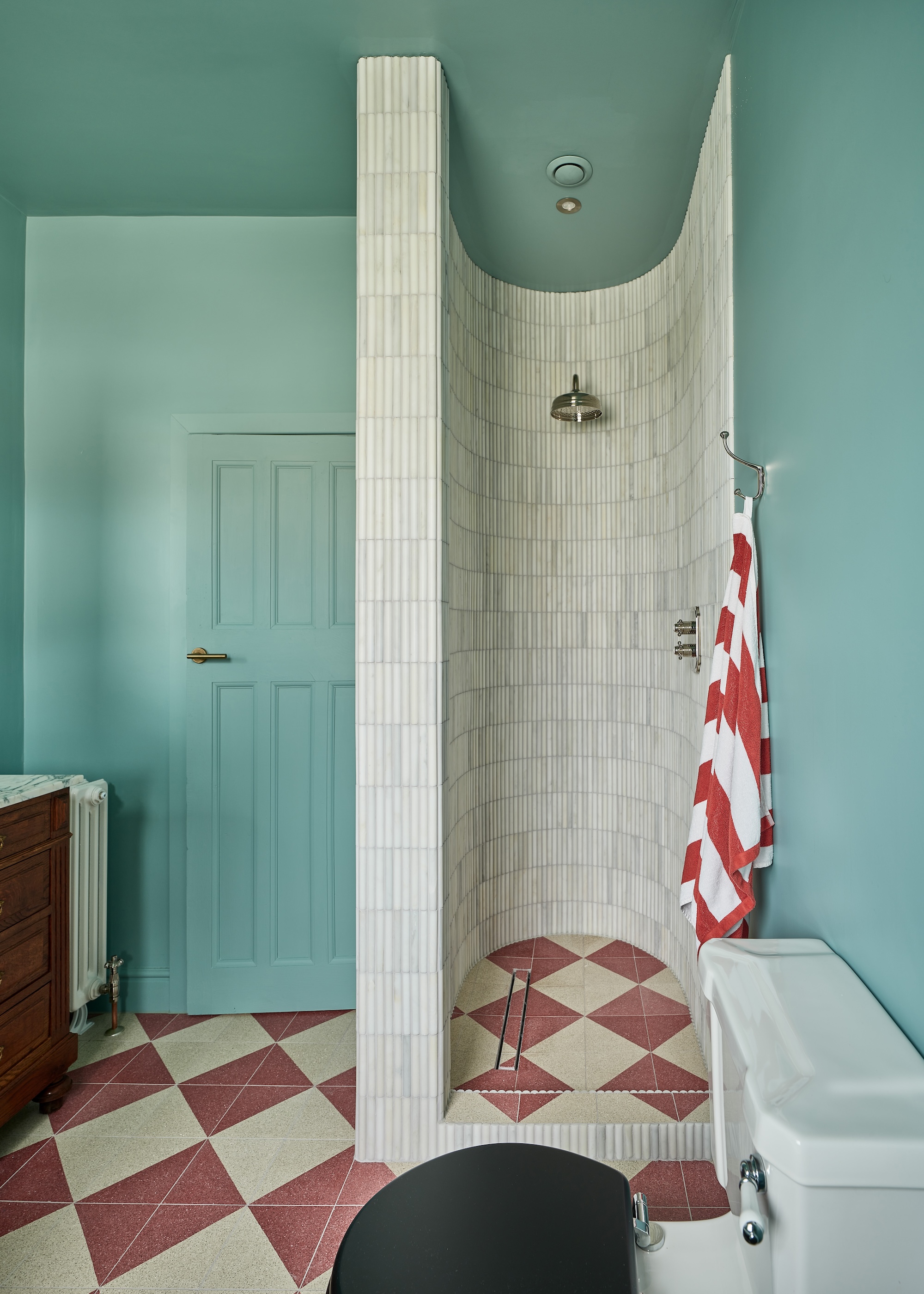 A curved shower in a baby blue painted room with checkered flooring.