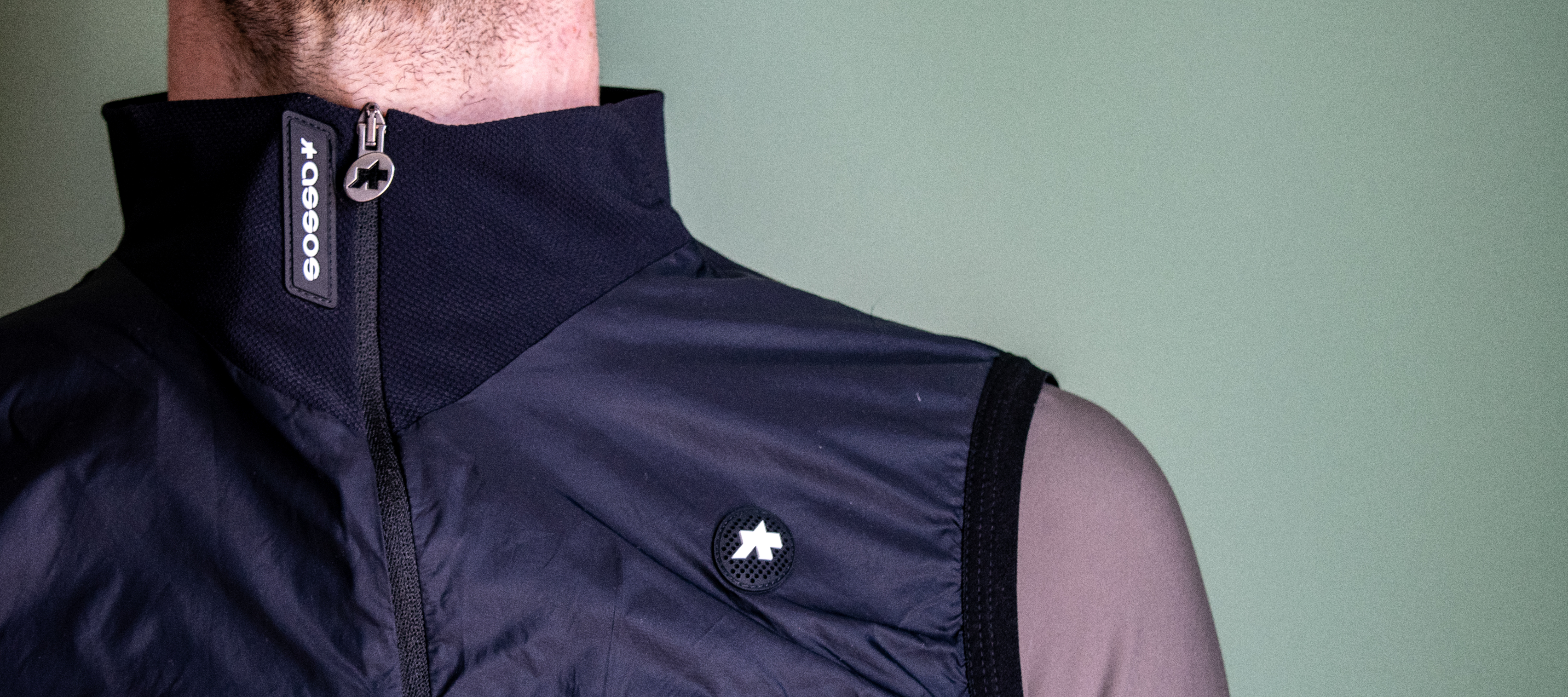 A man wearing a black Assos Tactica gilet over a grey long sleeve shirt