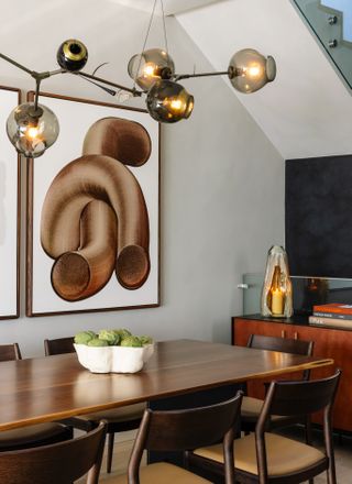 A grounded dining room with overhead hanging lighting and wall art