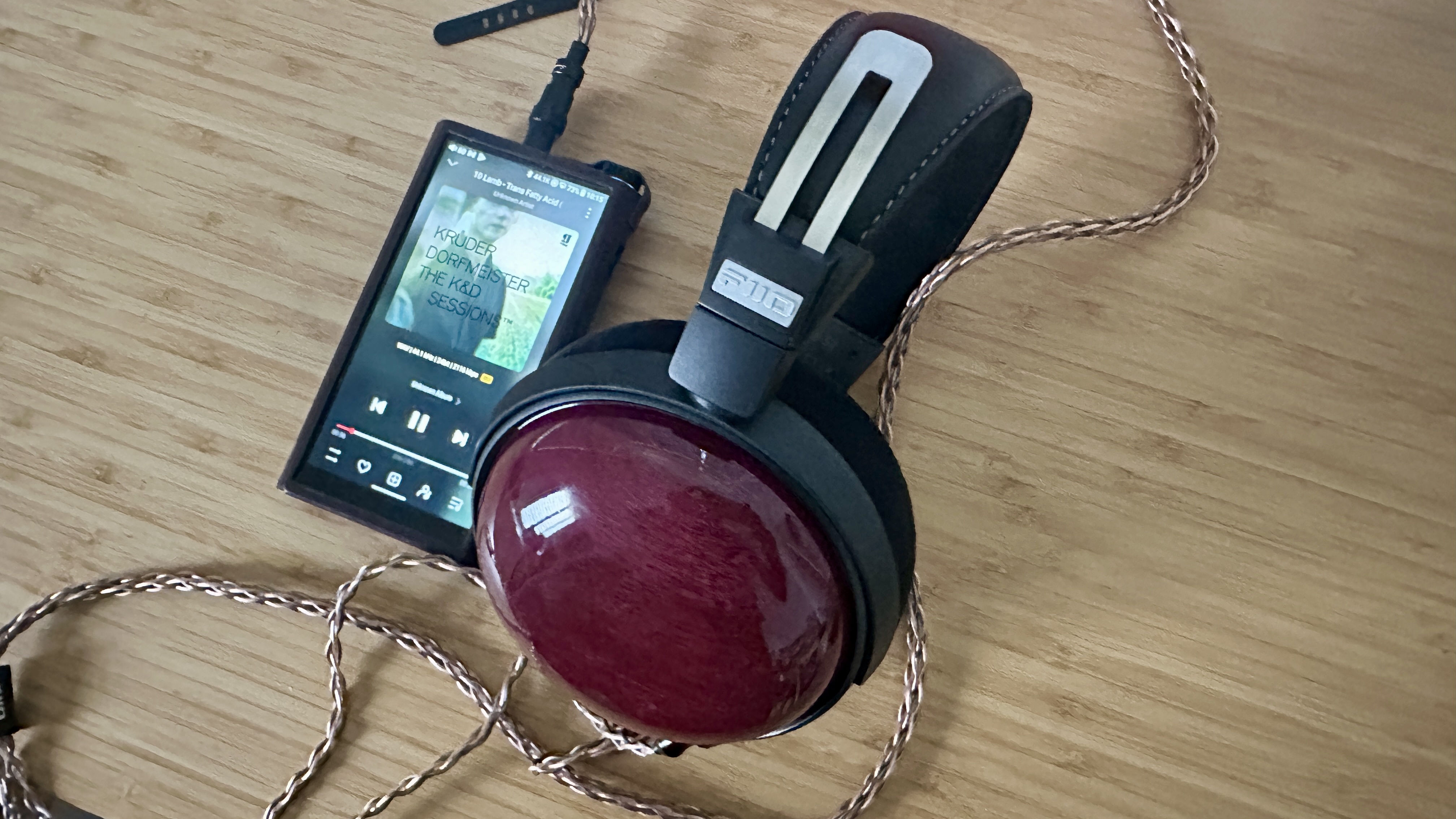 FiiO FT13 closed-back over-ear headphones plugged into a portable music player, on a wooden surface.