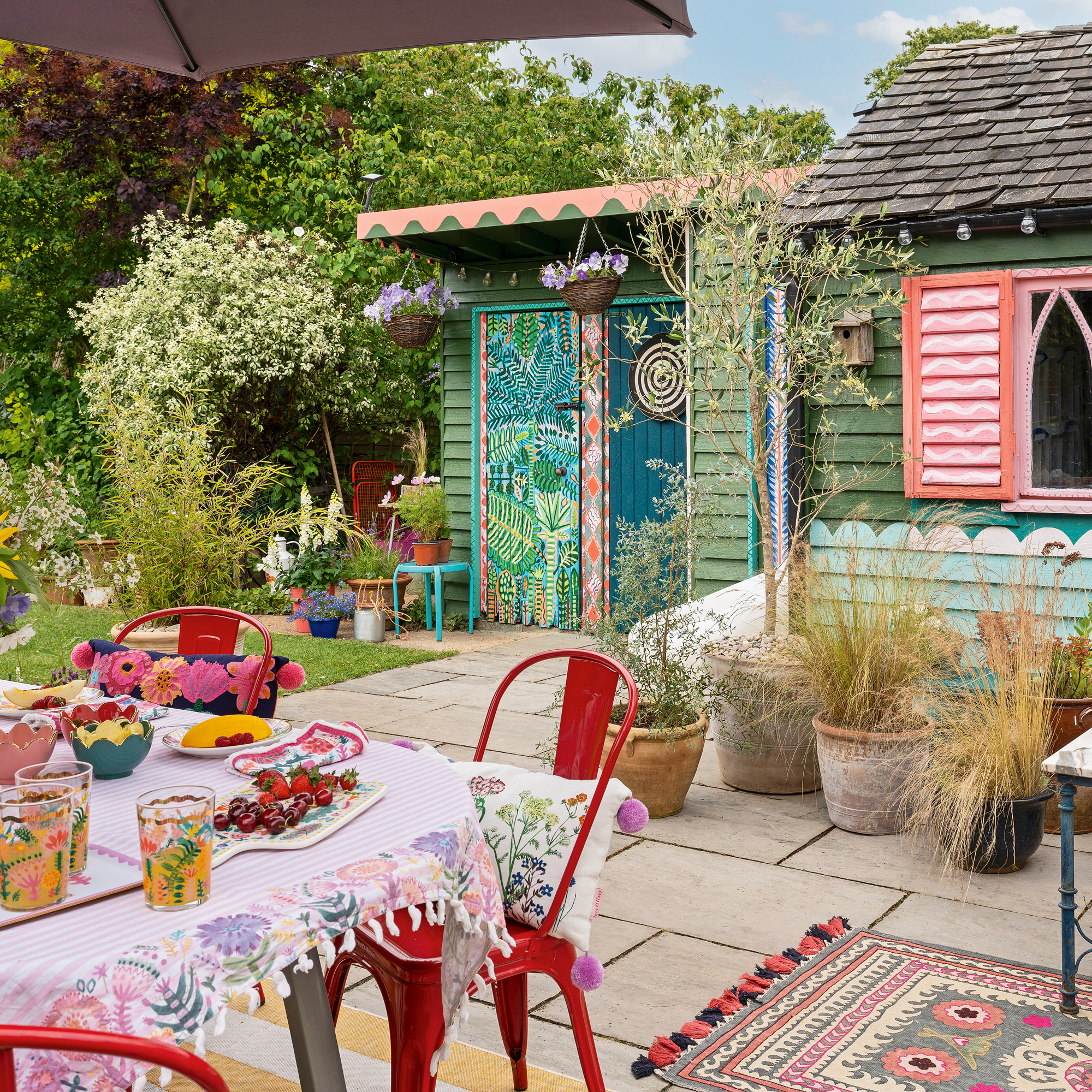 a garden with two brightly painted sheds with a dining table