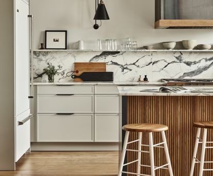 An organic modern kitchen with marble countertops and backsplash and beige slim style shaker cabinets