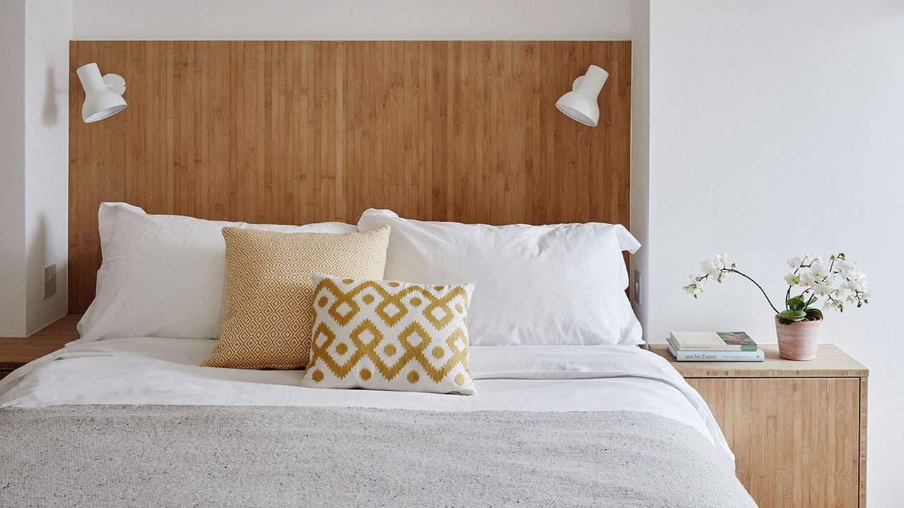 Made up bed with white sheets and built in reading lights in wooden headboard