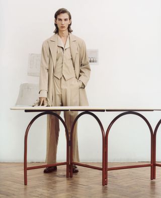 A man stands in beige clothes with his hands across a table