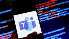 The Microsoft Teams logo displayed on a smartphone in front of a screen of red and blue computer code