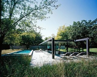 Alternative view of the outdoor area at The Highveld Pavilion during the day. There is a swimming pool, lounge chairs, a black and glass structure and greenery