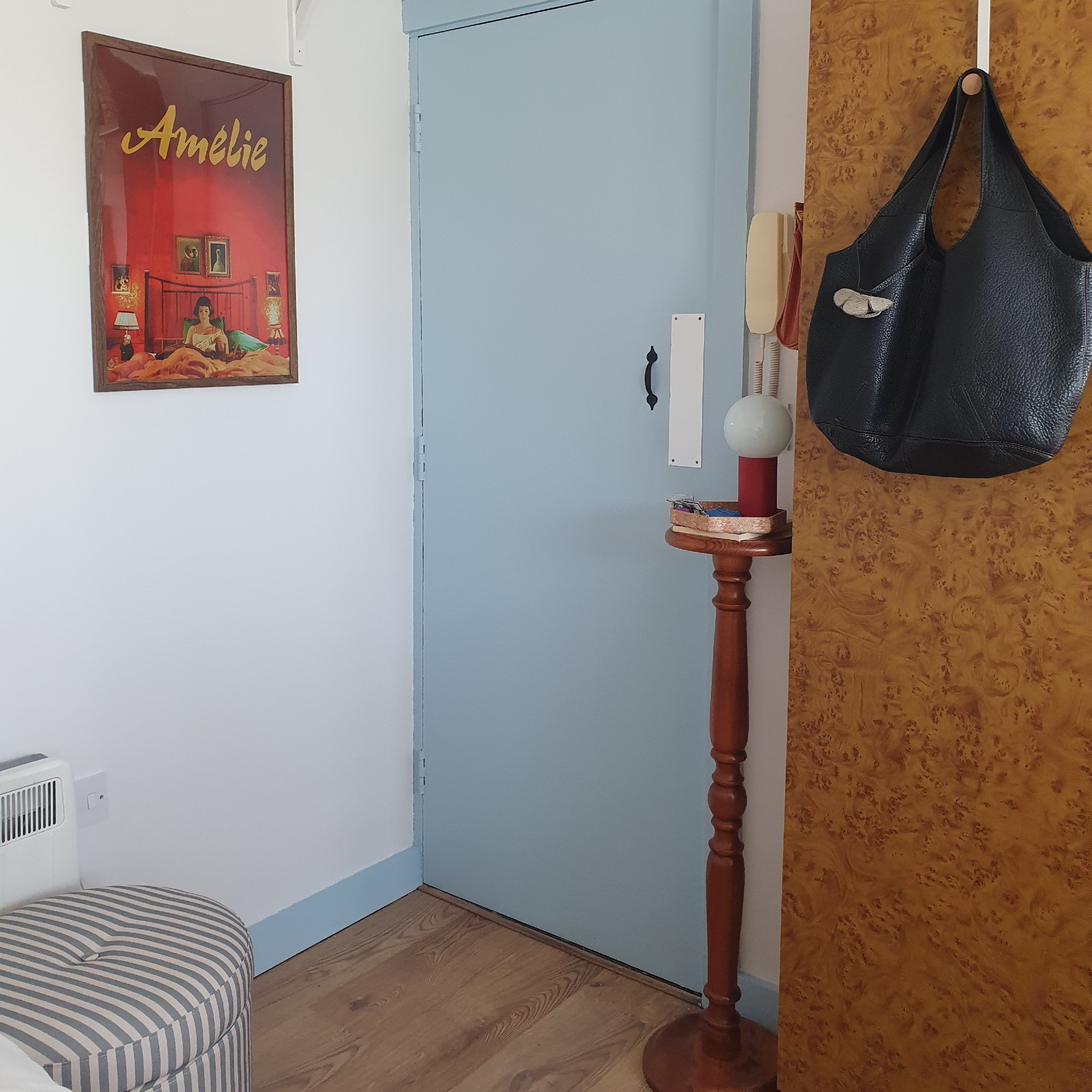 Sara's entrance area with a striped storage ottoman, a side table with a lamp next to the front door and a framed film poster hanging on the wall
