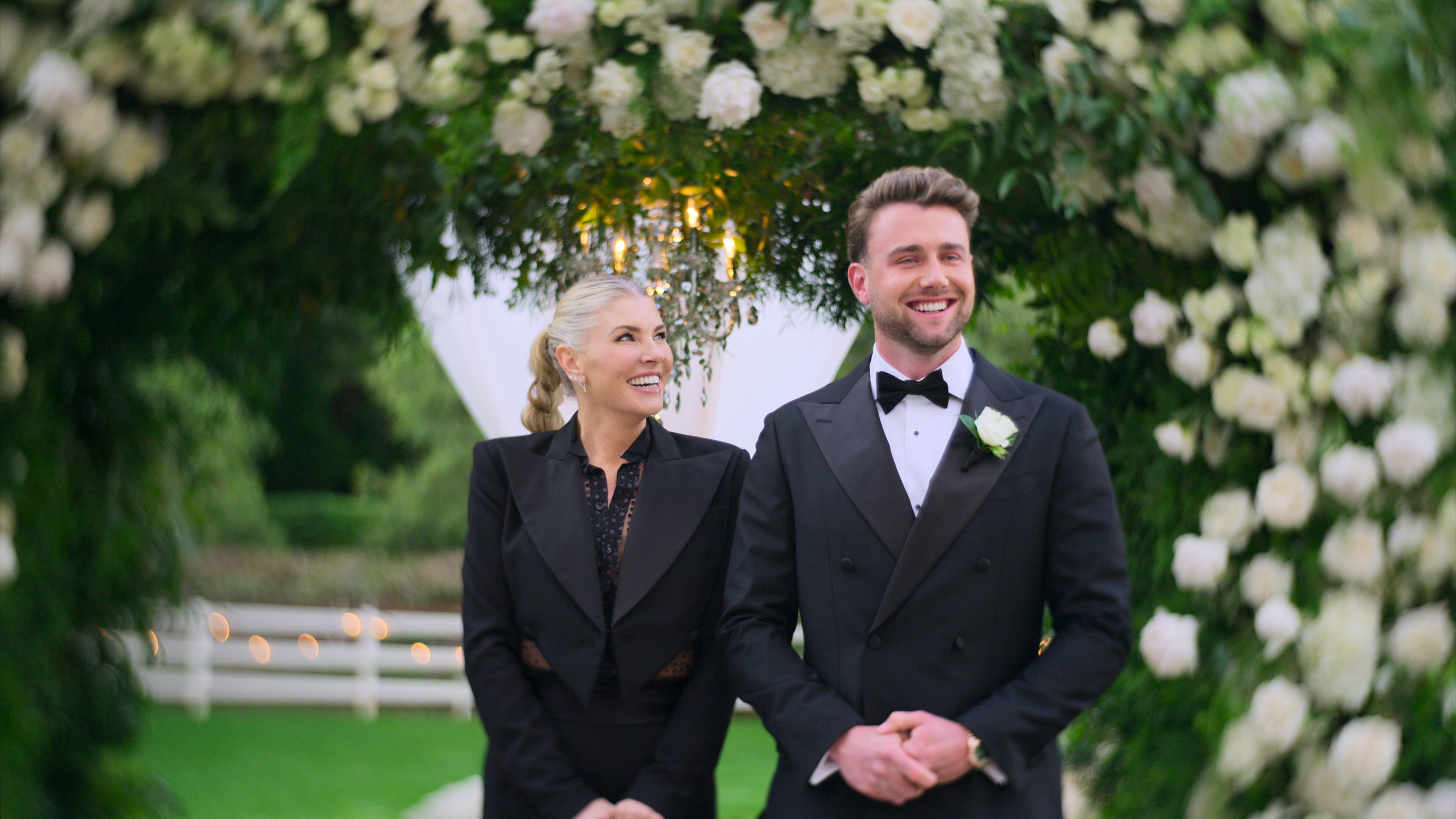 Amanda Kloots wears a black suit with her hair in a braid and stands next to Harry Jowsey wearing a tux on 'Let's Marry Harry.'