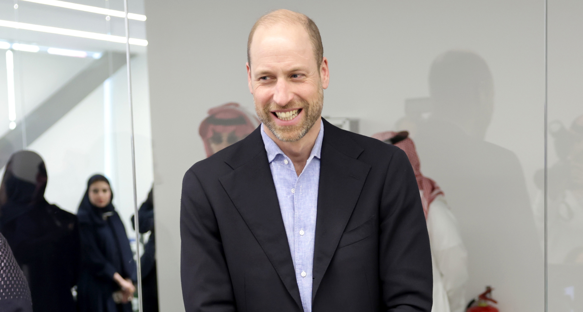 Prince William wearing a suit and laughing standing in a room with gamers