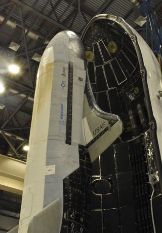 a white robotic space plane stands before the inner black shell of a white rocket fairing half ahead of USSF-52.