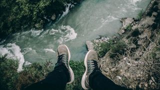 A person sits on a cliff over a river.