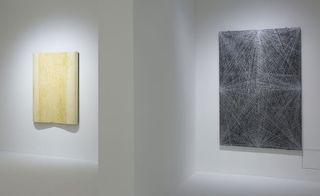 Two paintings hang against a white wall. One cream/yellow, and the other black with white converging lines