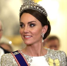 Kate Middleton wearing a tiara and white and silver evening dress looking to the left and smiling