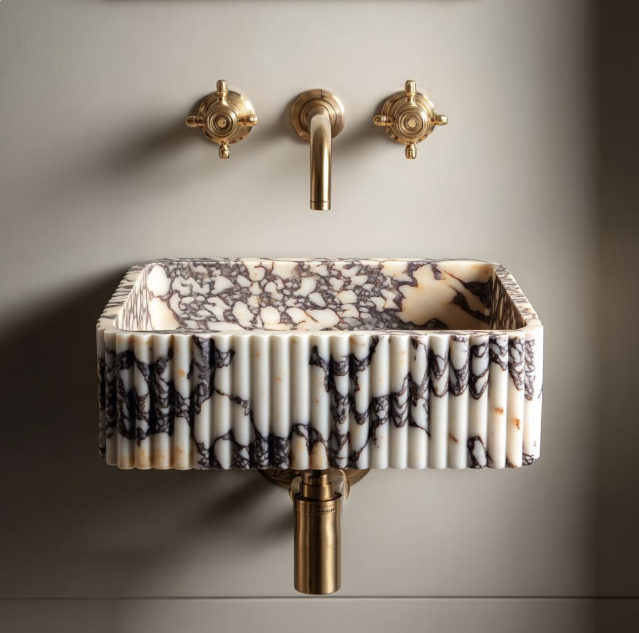 calacatta marble sink with gold hardware mounted on a grey wall
