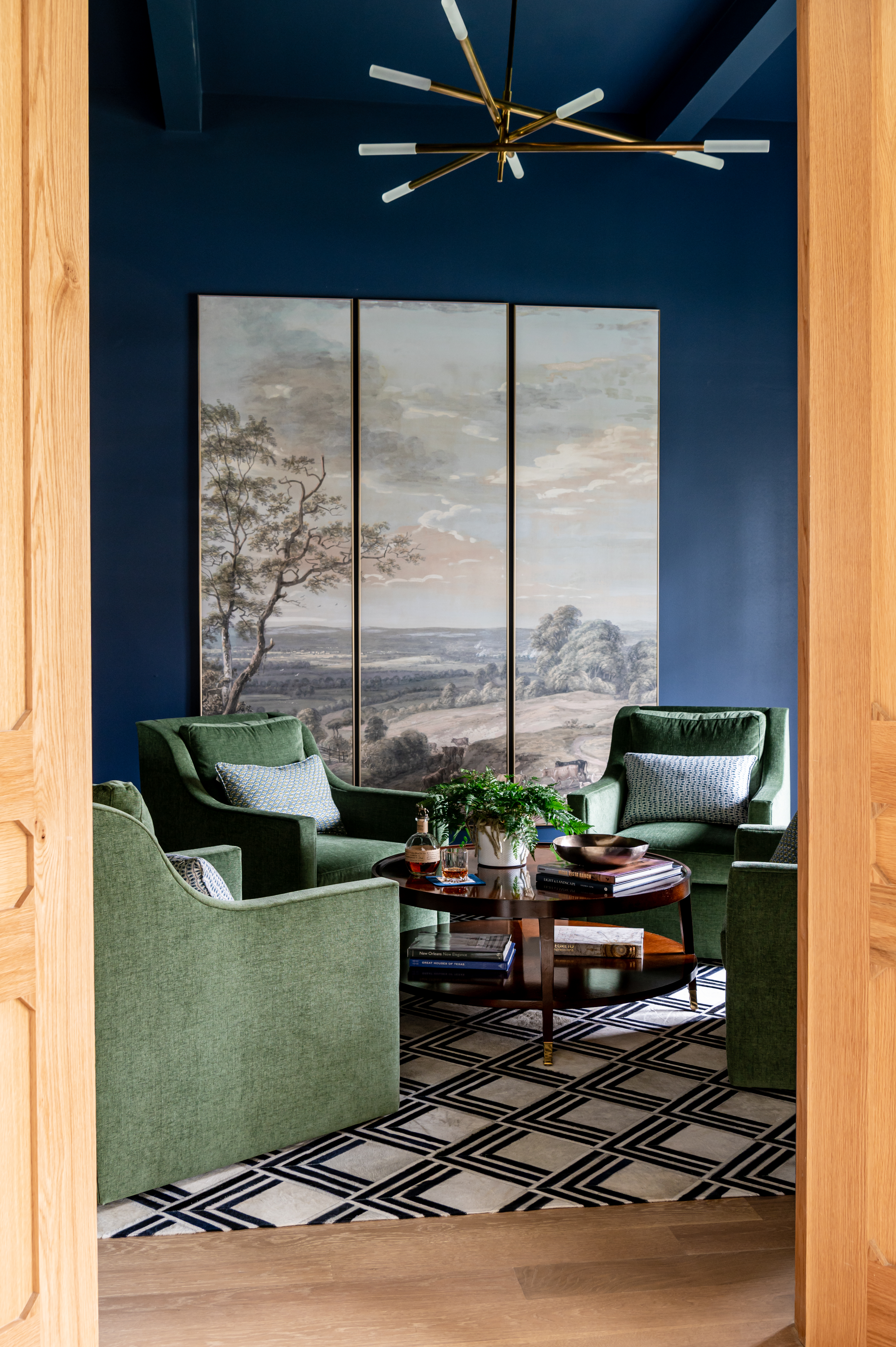 Navy blue sitting room with green accent chairs and a wooden coffee table. A triptych print is on the wall in the background.