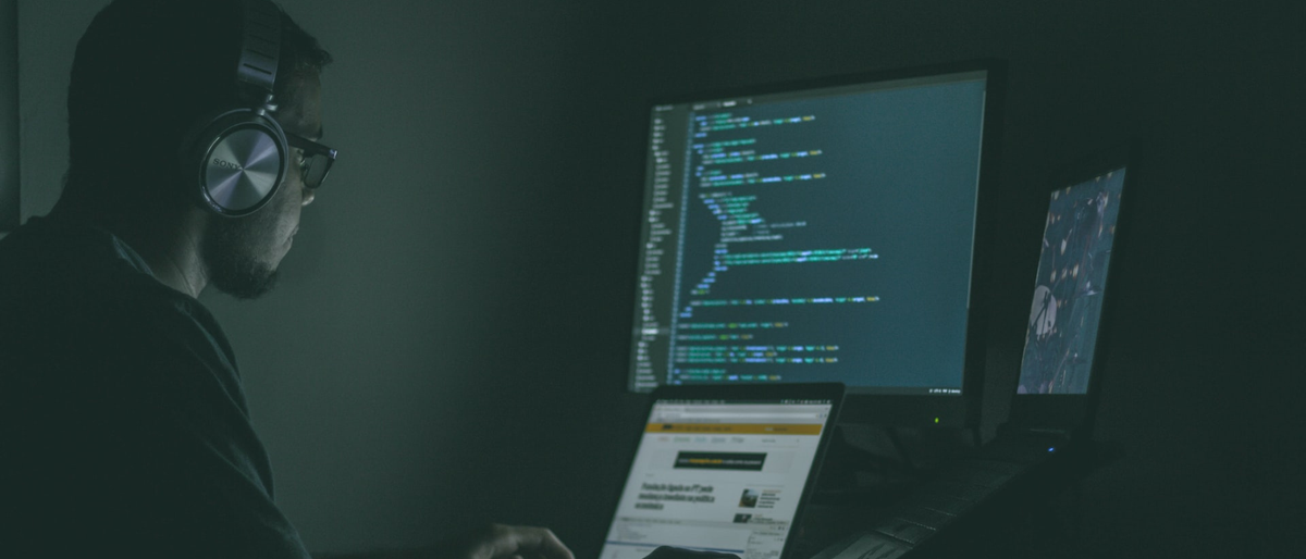 Man using a laptop and computer in a darkened home office